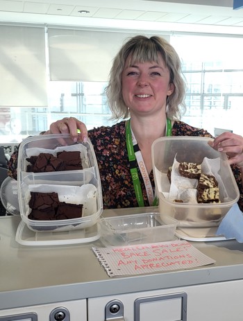 a photo of a member of staff holding cakes at the bake sale