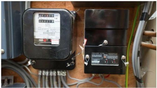 A black RTS meter and a black teleswitch box fastened to a chipboard wall, side by side