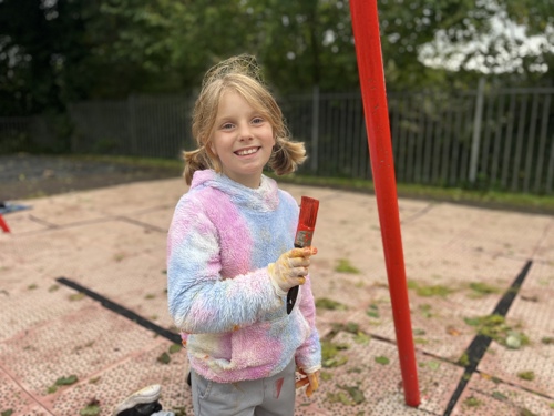 girl holding a paintbrush to show the playground equipment she was painting
