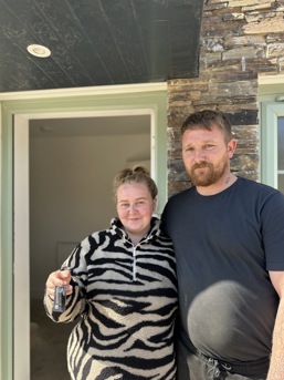 a photo of a couple, smiling in their doorway with the keys to their new home