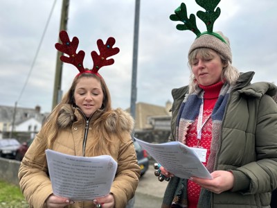 photo of two cornwall housing staff singing carols wearing festive headbands