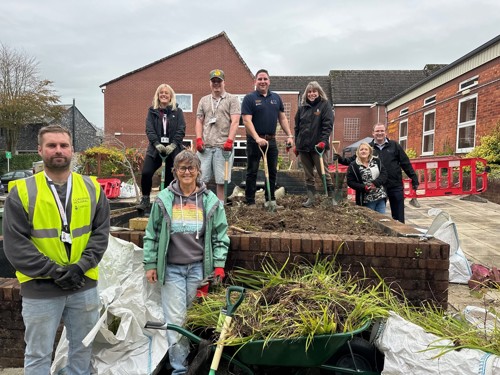 A group photo of staff from Cornwall Housing, Cardo and CCS standing infront of the fishpond they are transforming into a garden