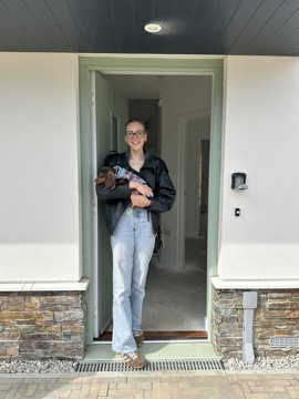 A photo of a new resident, Ellie, smiling and leaning in her doorway