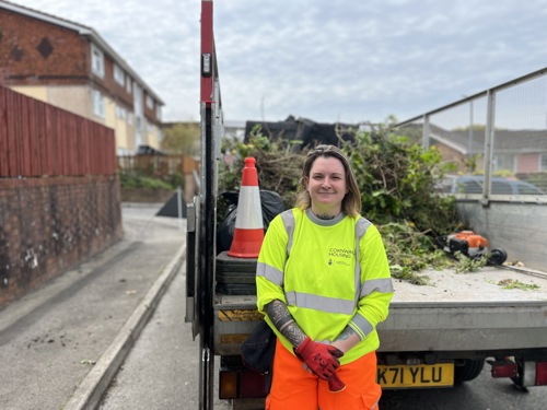 Female estate ranger stood by truck with garden waste on it in a cornwall housing neighbourhood